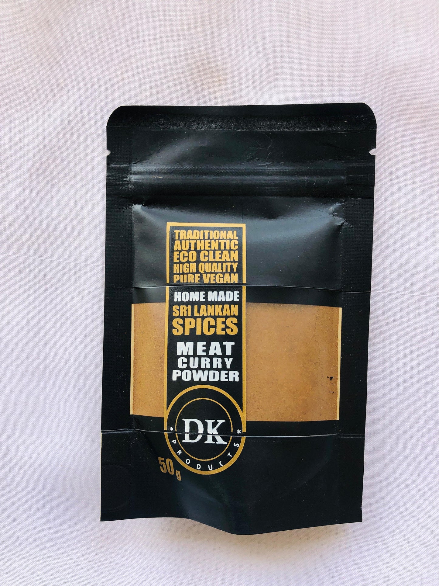 Black packaging of DK Home Made Sri Lankan Spices Meat Curry Powder on a light gray background